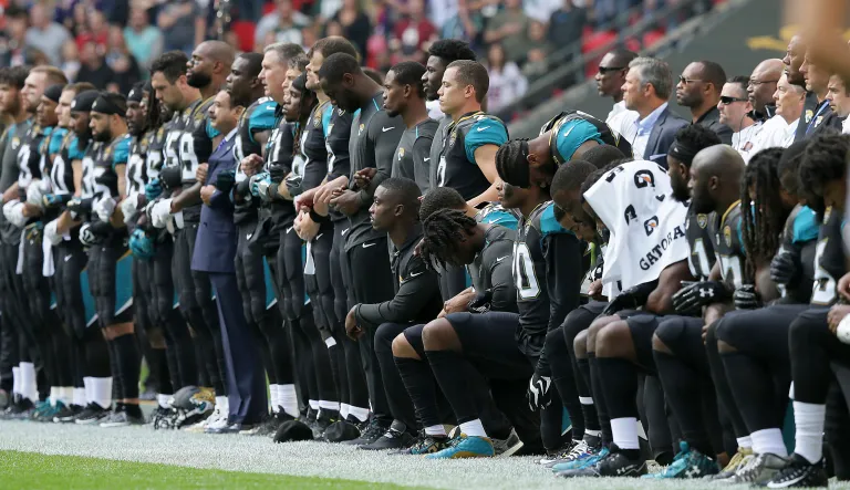 Jacksonville Jaguars players lock arms and kneel down during the playing of the U.S. national anthem before an NFL football game. The commander of a veterans group said, 