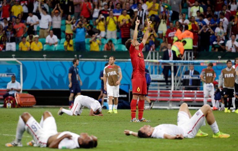 Exhausted US players lie on the ground as Belgium's Axel Witsel (6) celebrates at the end of the extra time during the World Cup round of 16 soccer match between Belgium and the USA at the Arena Fonte Nova in Salvador, Brazil, Tuesday, July 1, 2014. Belgium held on to beat US 2-1 in extra time.(AP Photo/Felipe Dana)