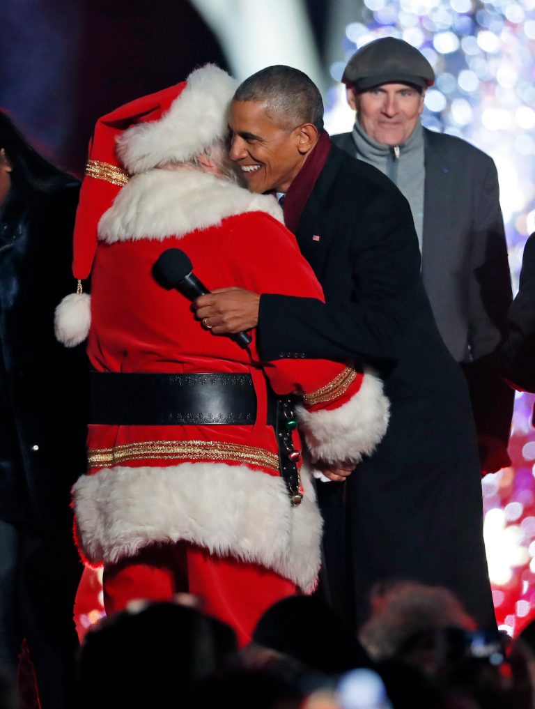 President Barack Obama, center, hugs Santa Claus, with James Taylor, right, during the lighting ceremony for the 2016 National Christmas Tree is seen before the lighting ceremony on the Ellipse near the White House, Thursday, Dec. 1, 2016 in Washington. (AP Photo/Alex Brandon)