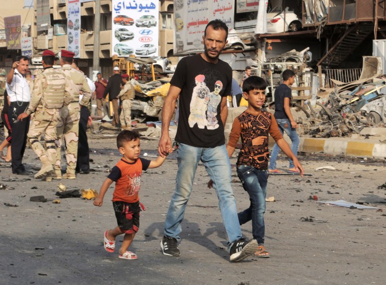 Civilians walk through the site of a car bomb explosion in the largely Shiite eastern neighborhood of Talibiyah in Baghdad, Iraq, Thursday, Oct. 16, 2014. A suicide bomber rammed his explosives-laden car into a police checkpoint Thursday in the Iraqi capital, killing more than 10 and wounding tens of people, Iraqi officials said. (AP Photo/Khalid Mohammed)