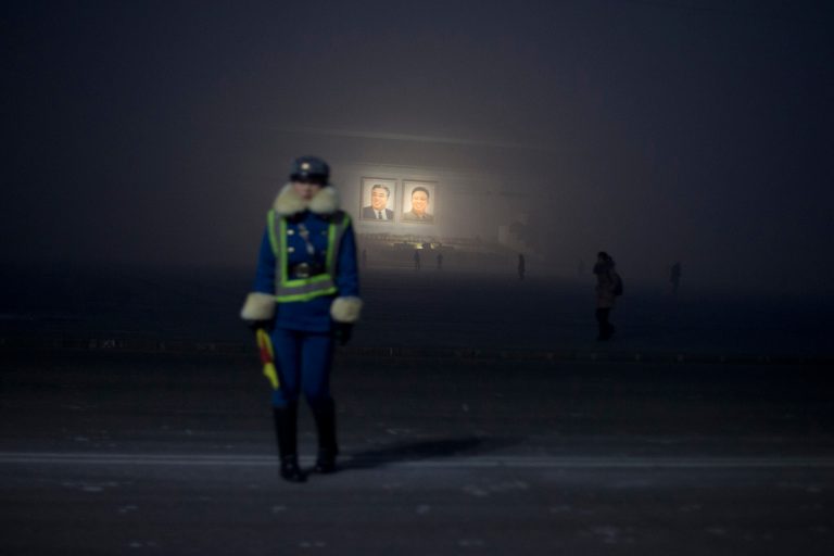   A North Korean traffic coordinator stands on a roadside near portraits of the late leaders Kim Il Sung, left, and Kim Jong Il during a foggy morning on Kim Il Sung Square in Pyongyang, North Korea, Monday, Dec. 17, 2012. North Korea marked the first death anniversary of the former leader Kim Jong Il on Monday. (AP Photo/Ng Han Guan)  