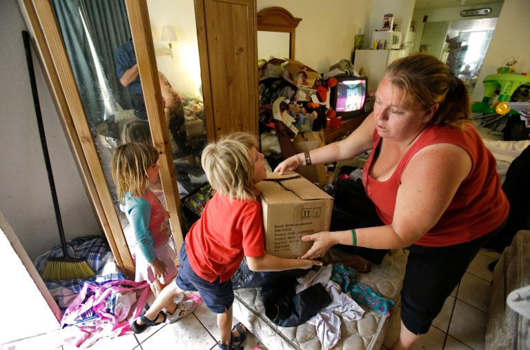 In this Tuesday, April 8, 2014 photo, Theresa Muller hands a box of times to her son Timothy, 7, with her daughter Mikenzie, 4, as she moves out of her motel room she shares with her boyfriend, father and three children in Kissimmee, Fla. Muller and her family have been homeless but plan to move to a home in a neighboring county.(AP Photo/John Raoux)