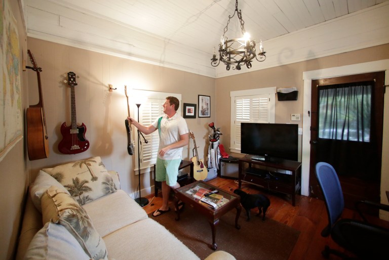 In this July 30, 2014 photo, Renter Matthew Clarie hangs a guitar in the living room of his 388-square-foot home in Hyde Park, Fla. Tom Scarritt, 57, a lawyer, bought the home with his wife, Linda, a decade ago, convinced it would make a good one-room rental for 
