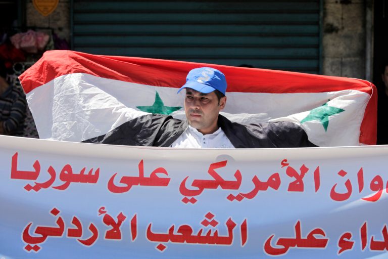   A Jordanian man holds the Syrian national flag during a protest by the Jordanian Communist Party and other leftist groups against any American military strike against Syria, in Amman, Jordan, Friday, Aug. 30, 2013. The Arabic banner reads 