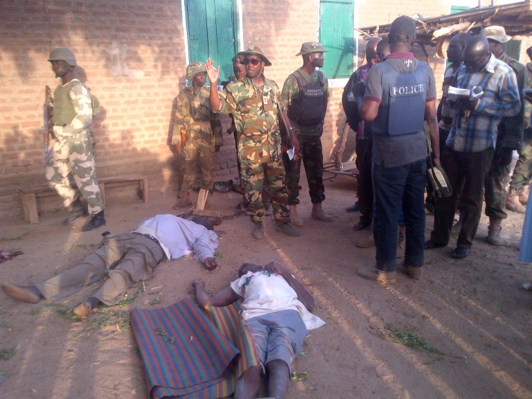 In this photo taken with a mobile phone, Tuesday, May. 7, 2013, soldiers and journalist looks at bodies of prison officials killed by Islamic extremist during heavy fighting in Bama, Nigeria. Coordinated attacks by Islamic extremists armed with heavy machine guns killed at least 42 people in northeast Nigeria, authorities said Tuesday, the latest in a string of increasingly bloody attacks threatening peace in Africa's most populous nation. The attack struck multiple locations in the hard-hit town of Bama in Nigeria's Borno state, where shootings and bombings have continued unstopped since an insurgency began there in 2010. Fighters raided a federal prison during their assault as well, freeing 105 inmates in another mass prison break to hit the country, officials said. (AP Photo/Abdukareem Haruna)