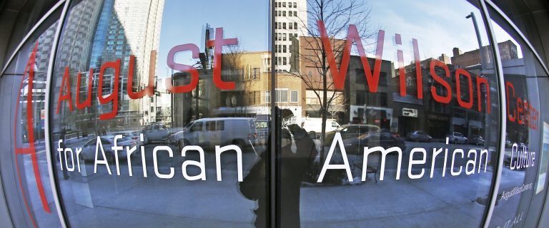 This photo made with a fisheye lens on Thursday, Jan. 30, 2014, shows buildings and traffic along Liberty Ave. in Pittsburgh that are reflected in the windows with the signage for the August Wilson Center for African American Culture. The center may soon be sold to pay off millions in debt, and some experts say it's a telling reflection on the difficulties of promoting theatre and black culture in America. (AP Photo/Keith Srakocic)