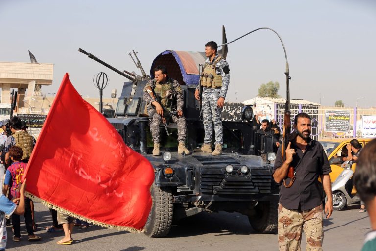Iraqi federal policemen watch as Shiite tribal fighters deploy with their weapons in the northwest Baghdad's Shula neighborhood, Iraq, Monday, June 16, 2014. Sunni militants captured a key northern Iraqi town along the highway to Syria early on Monday, compounding the woes of Iraq's Shiite-led government a week after it lost a vast swath of territory to the insurgents in the country's north. (AP Photo/Karim Kadim)