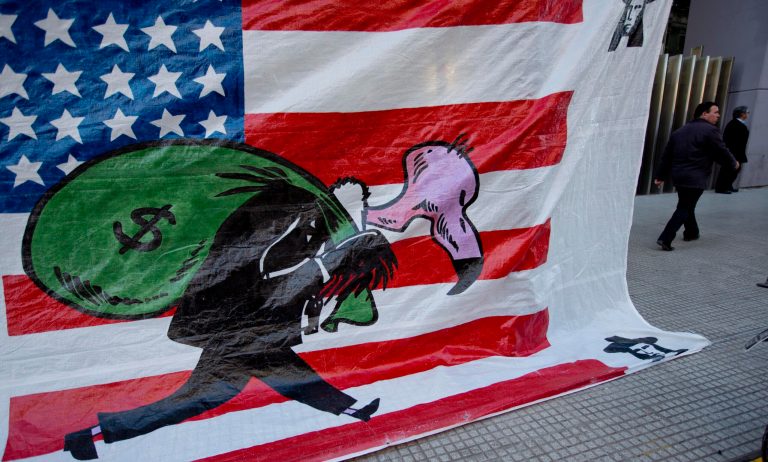 A banner shows a vulture, symbolizing a U.S. hedge fund, carrying a bag of money in front of the U.S. flag outside Congress in Buenos Aires, Argentina, Wednesday, Sept. 10, 2014. Congress is expected to vote on a bill, that if approved, would allow Argentina to pay creditors locally in Argentina. Argentina was forced into a second default on July 30 following a decade-long legal battle with U.S. investors including hedge funds who refused to accept lower payments for bonds that the South American country defaulted on in 2001. The investors obtained a U.S. court order, preventing Argentina from making interest payments which triggered the second default. (AP Photo/Natacha Pisarenko)