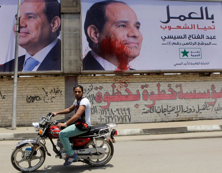 An Egyptian rides his motor bike past campaign banners for presidential hopeful retired Field Marshal Abdel-Fattah el-Sissi, one of which splashed with red paint in Cairo, Egypt, Thursday, May 22, 2014. Arabic reads, 