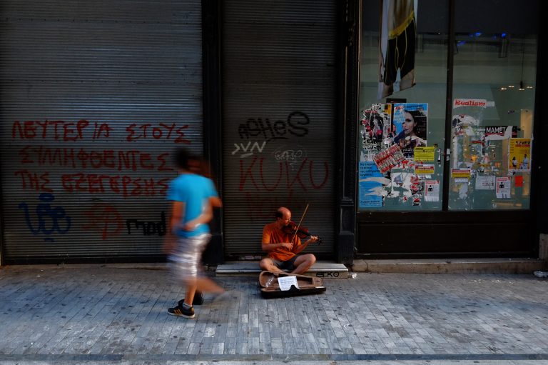 A musician plays violin as a couple walks past at a main shopping street outside of an empty closed shop in central Athens, Monday, June 30, 2014. After a crippling six-year recession lopped a quarter off the economy, Greece is expected to return to modest growth by the end of this year, according to many financial experts. The country has relied on international bailouts since it nearly went bankrupt in 2010.(AP Photo/Petros Karadjias)