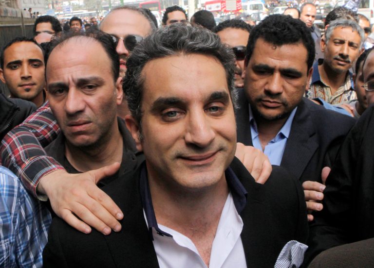 FILE - In this Sunday, March 31, 2013 file photo, a bodyguard secures popular Egyptian television satirist Bassem Youssef, who has come to be known as Egypt's Jon Stewart, as he enters Egypt's state prosecutors office to face accusations of insulting Islam and the country's Islamist leader in Cairo, Egypt. Egypt's state Investment Authority said Tuesday, April 2, 2013 it will revoke the license of a private TV station that airs a popular satirist if he does not stop the use of 