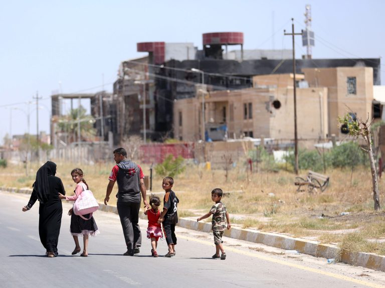 In this Sunday, June 21, 2015 photo, a displaced family walks towards their home in Tikrit, 80 miles (130 kilometers) north of Baghdad, Iraq. Civilians are trickling back into Saddam Hussein's hometown as they look to start anew, the consequences of a year under Islamic State rule conspicuously written on its charred buildings and damaged homes. (AP Photo/ Hadi Mizban)