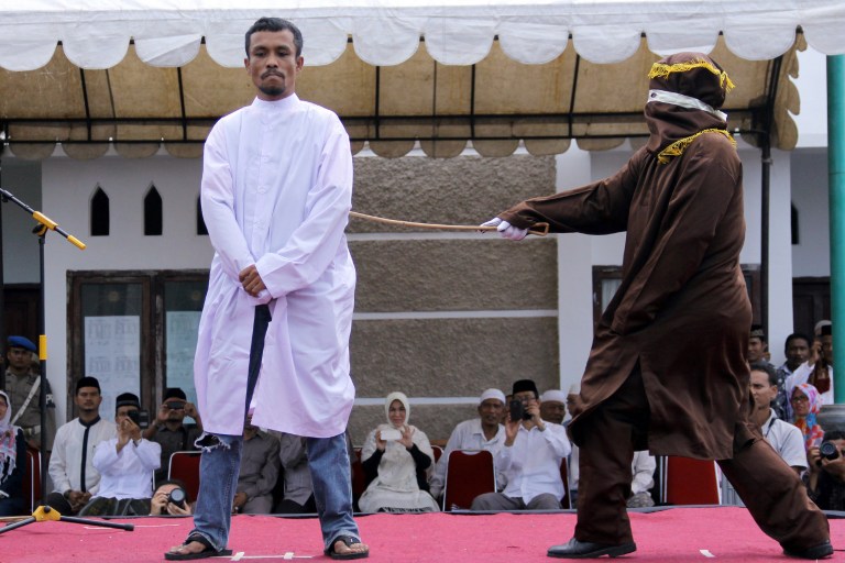 An Islamic Shariah law official whips a man, convicted of gambling, with a rattan cane watched by people inside a mosque compound in Banda Aceh, Aceh Province, Indonesia, Friday, Oct 3, 2014. Indonesian authorities publicly caned four men who were convicted of gambling in conservative Aceh province after Friday prayers. (AP Photo/Heri Juanda)