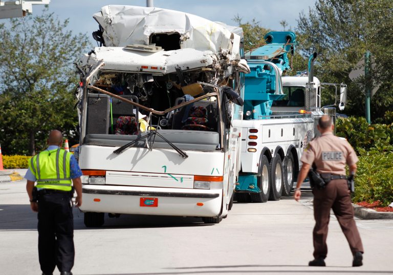   Law enforcement officers watch as a bus which hit a concrete overpass at Miami International Airport is hauled away, Saturday, Dec. 1, 2012 in Miami. The vehicle was too tall for the 8-foot-6-inch entrance to the arrivals area, and buses are supposed to go through the departures area which has a higher ceiling, according to an airport spokesperson. (AP Photo/Wilfredo Lee) (AP Photo/Wilfredo Lee)  