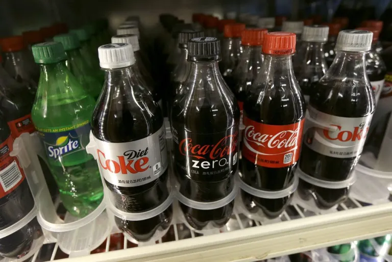 A shelf of soft drinks are shown in a refrigerator.