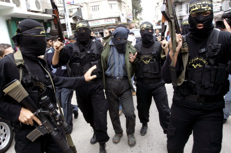 FILE - In this Sunday Nov. 5, 2006 file photo, Palestinian Islamic Jihad masked gunmen hold up their guns as they display one of two men whom they alleged were Palestinian collaborators for Israel in Gaza City. Hamas views collaborators in Gaza as a serious threat, holding them responsible for the assassination by Israel over the years of dozens of its top political leaders and military commanders. Israel, on the other hand, has historically relied on collaborators in its war against Palestinian militants and Palestinian activism in general, using methods that vary from entrapment and blackmail to cash and perks. (AP Photo/Khalil Hamra, File)