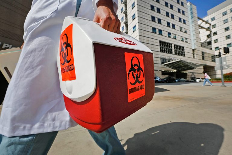 A research assistant with the David Geffen School of Medicine at UCLA carries a portable cooler marked with a biohazard label past the Ronald Reagan UCLA Medical Center in Los Angeles, Thursday, Feb. 19, 2015. (AP Photo/Damian Dovarganes)