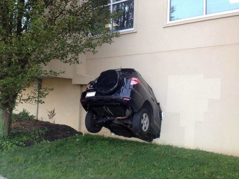 In this photo provided by the Baltimore County Police, an SUV hangs out of the side of a building that houses county offices after its driver drove into the building, injuring three people, Thursday, July 31, 2014, in Towson, Md. The driver was charged with failure to reduce speed to avoid a collision. (AP Photo/Baltimore County Police, Elise Armacost)