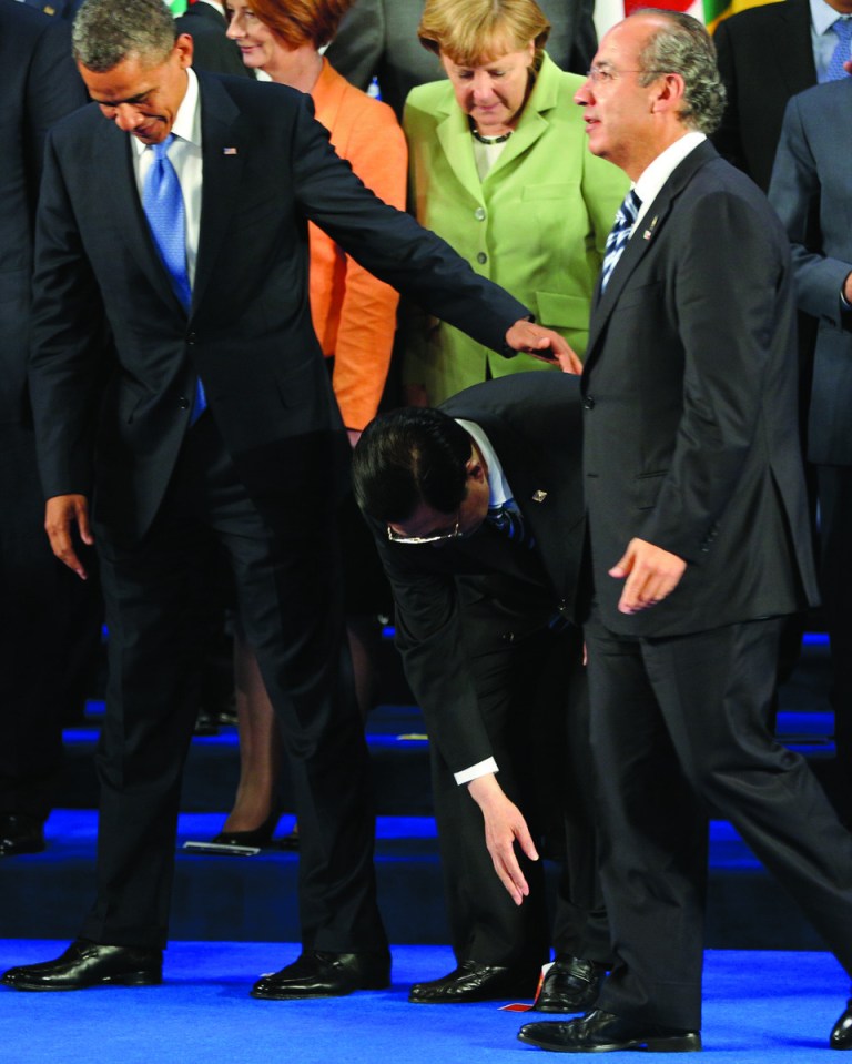 President Barack Obama, left, assists China's President Hu Jintao, center, as the flag who marked his position in the stage got stick to his shoe while Mexico's President Felipe Calderon walks by and Germany's Chancellor Angela Merkel looks on after posing for the family photo of the G-20 Summit in Los Cabos, Mexico, Monday, June 18, 2012. (AP Photo/Andres Leighton)