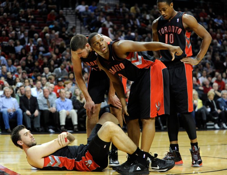   Toronto Raptors' Andrea Bargnani, left, holds his elbow as teammates gather around during the first half of an NBA basketball game against the Portland Trail Blazers in Portland, Ore., Monday, Dec. 10, 2012. (AP Photo/Greg Wahl-Stephens)  