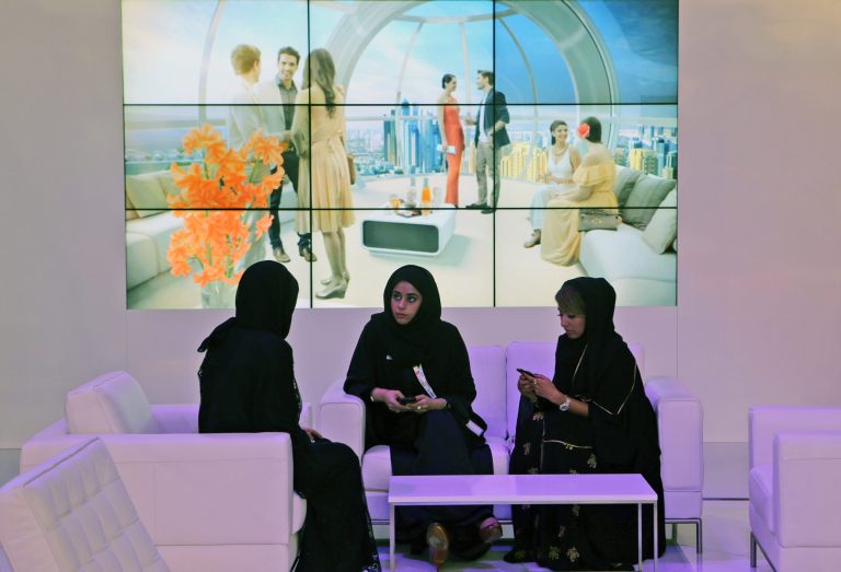 FILE - In this Wednesday, Oct. 9, 2013 file photo, Emirati staff members of the Bluewaters Island project talk to each other in front of a video screen to promote the project during the second day of a real estate fair called Cityscape Global in Dubai, United Arab Emirates. The United Arab Emirates is finalizing a new law that gives broad incentives to entrepreneurial citizens as part of a wider race against time to create jobs for a burgeoning young population. (AP Photo/Kamran Jebreili, File)