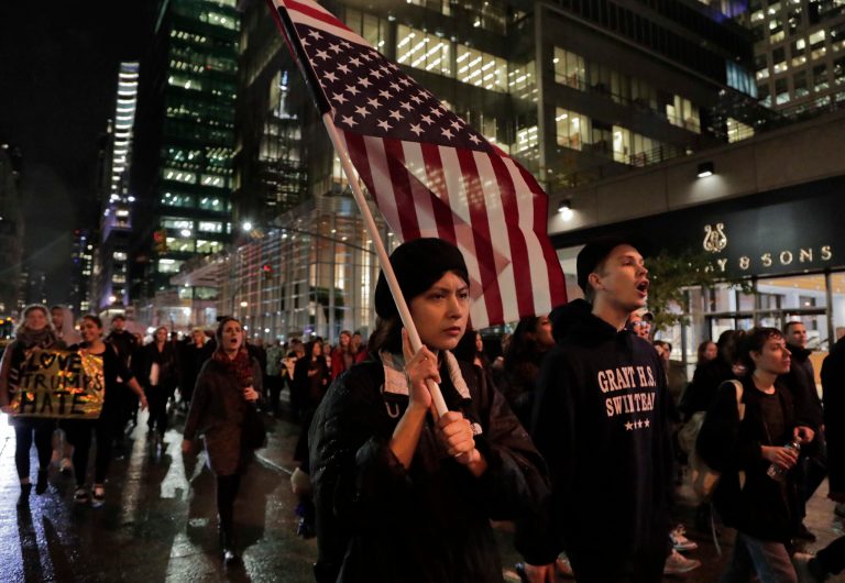 A protester carries an upside down American flag as she walks along Sixth Avenue while demonstrating against President-elect Donald Trump, Wednesday, Nov. 9, 2016, in New York. Thousands of protesters around the country took to the streets Wednesday to condemn the election of Trump as president. (AP Photo/Julie Jacobson)