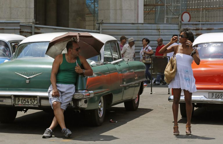 A taxi driver shades himself with an umbrella as he watches a woman prepare to cross the street near Central Park in downtown in Havana, Cuba, Saturday, May 16, 2015. (AP Photo/Desmond Boylan)