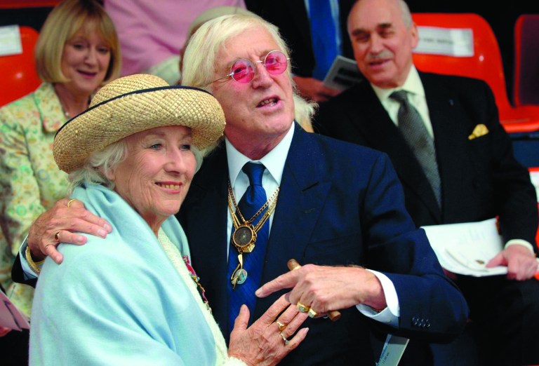 FILE In this Sunday Sept. 18, 2005 file photo British singer Vera Lynn and Jimmy Saville, right are seen at the unveiling of a contemporary sculpture at Victoria Embankment in central London to mark the 65th anniversary of the Battle of Britain. For decades, Jimmy Savile was a fixture on British television -- an eccentric, aggressively jocular host of children's shows and a tireless charity fundraiser. A year after he died, aged 84 and honored as Sir Jimmy, several women have come forward to claim he was also a sexual predator and serial abuser of underage girls. The allegations have set off ripples of shock -- but not of surprise. There had, colleagues said, long been rumors. The main question being asked now is: Why did no one do anything? (AP Photo/Matthew Fearn, Pool, File)