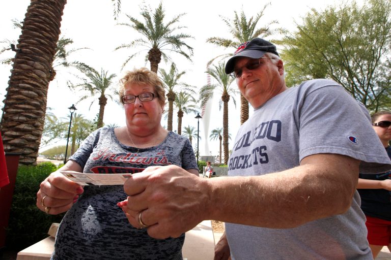 In this photo taken Wednesday, Feb. 26, 2014, Sue Knieriemen, of Fremont, Ohio, and her brother Charles Bork, of Sylvania, Ohio, check their tickets outside Goodyear Ballpark before an exhibition baseball game between the Cincinnati Reds and the Cleveland Indians in Goodyear, Ariz. After such a long, cold season, Americans across the winter-weary Midwest and the East Coast are desperate to escape to warm-weather destinations in California, Arizona and Florida. (AP Photo/Paul Sancya)
