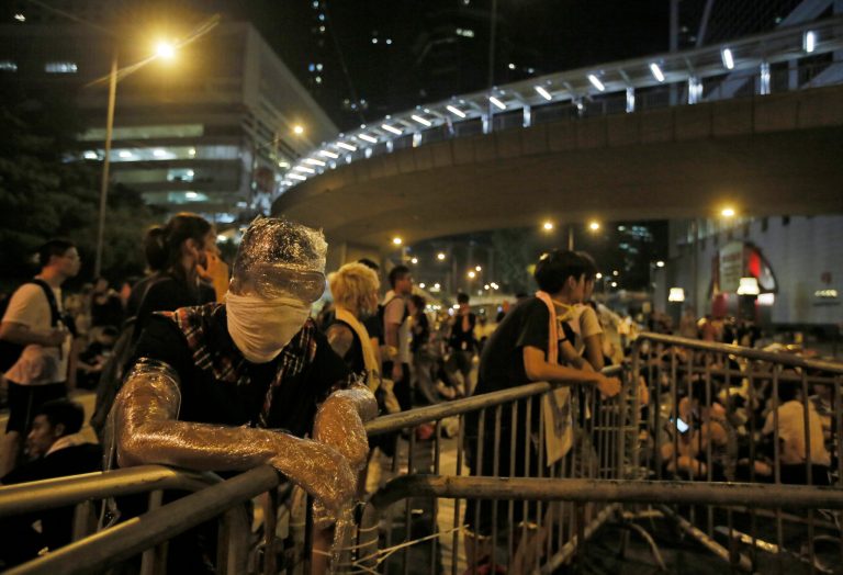 Wrapped in plastic to shield from pepper spray, a student protester stands behind a makeshift barrier blocking main streets in the central business district of Hong Kong, late Monday, Sept. 29, 2014. Pro-democracy protesters expanded their rallies throughout Hong Kong on Monday, defying calls to disperse in a major pushback against Beijing's decision to limit democratic reforms in the Asian financial hub. (AP Photo/Vincent Yu)