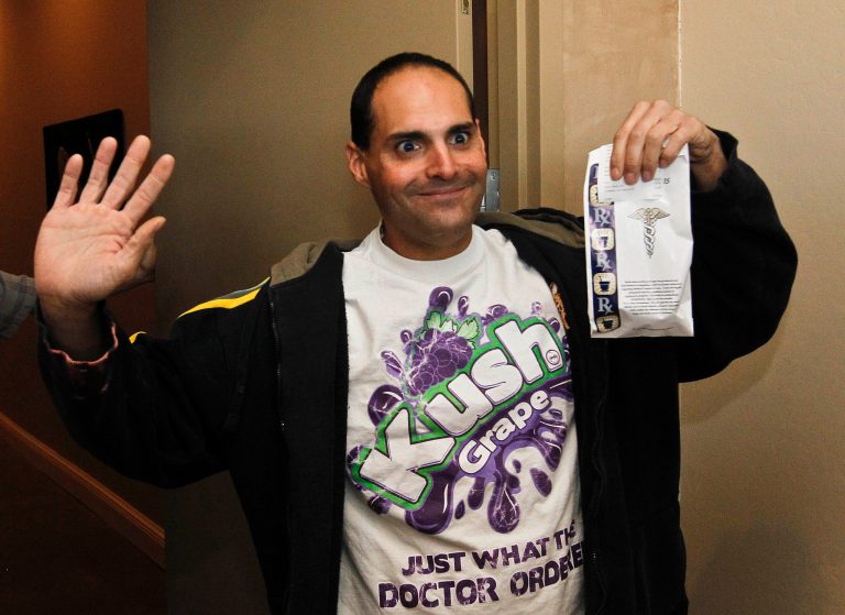   Mike Gonzalez, the first customer at Arizona Organix, reacts for the media as he holds up his medical marijuana purchase at Arizona Organix, the first legal medical marijuana dispensary to open in Arizona, Thursday Dec. 6, 2012, in Glendale, Ariz. Several dozen waited outside for the Glendale dispensary to open, the first among 96 applicants chosen through a lottery system for 126 geographic areas across the state.(AP Photo/Ross D. Franklin)  
