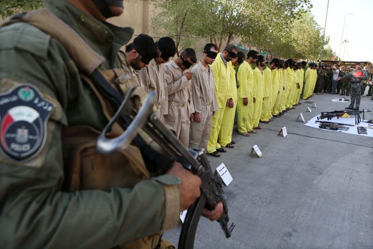A member of Iraq's Special Weapons and Tactics Team stands guard as blindfolded suspected terrorists are displayed at the federal police headquarters in Basra, Iraq, Sunday, July 20, 2014. Iraq's SWAT arrested 21 suspected terrorists during recent security operations in Basra, according to police. (AP Photo/Nabil al-Jurani)