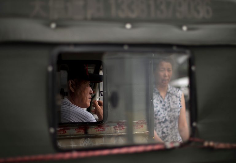 A Chinese man smokes inside his tricycle  as he waits for customer outside a shopping mall in Beijing, China Wednesday, July 16, 2014. China's economic growth edged up in the latest quarter and more than 7 million new jobs were created in the first half of the year, easing pressure on communist leaders as they try to prevent a precipitous slowdown in the world's second-largest economy. (AP Photo/Andy Wong)