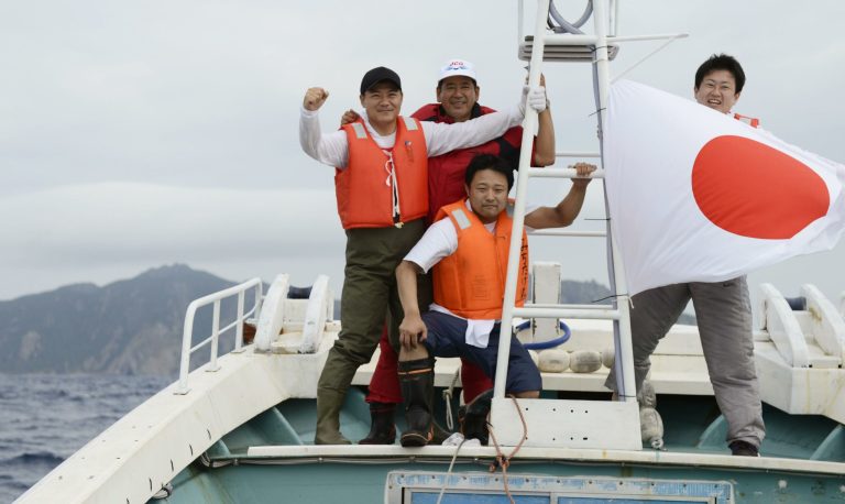   The ruling Democratic Party of Japan lawmakers, Tsutomu Takamura, left in background, Koichi Mukoyama, second left in background, and Yoichiro Morioka, foreground, pose on a fishing boat with the disputed islands in the East China Sea, which are called Senkaku in Japanese and Diaoyu in Chinese, as a backdrop during an unofficial 