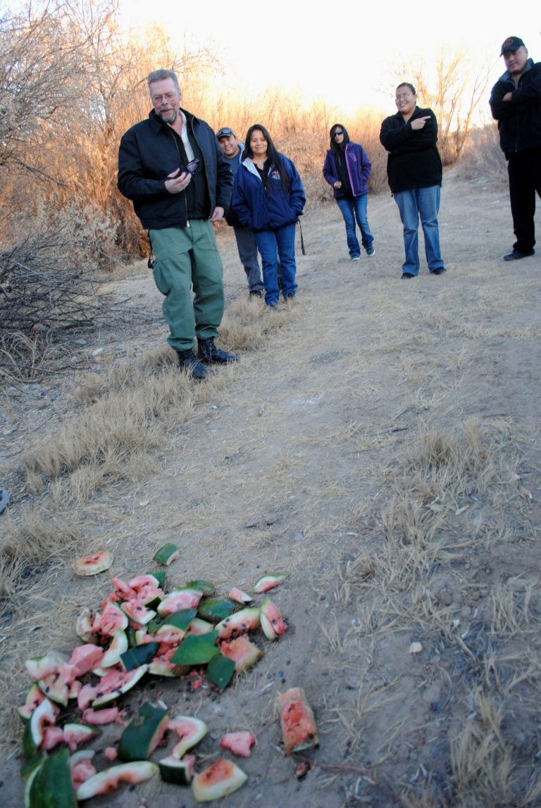   In this photo taken Saturday, Dec. 8, 2012, locals share stories of some of the odd creatures that they claim to have seen while they stand around a watermelon that an Upper Fruitland, N.M. resident cut up and left in the road for a local 