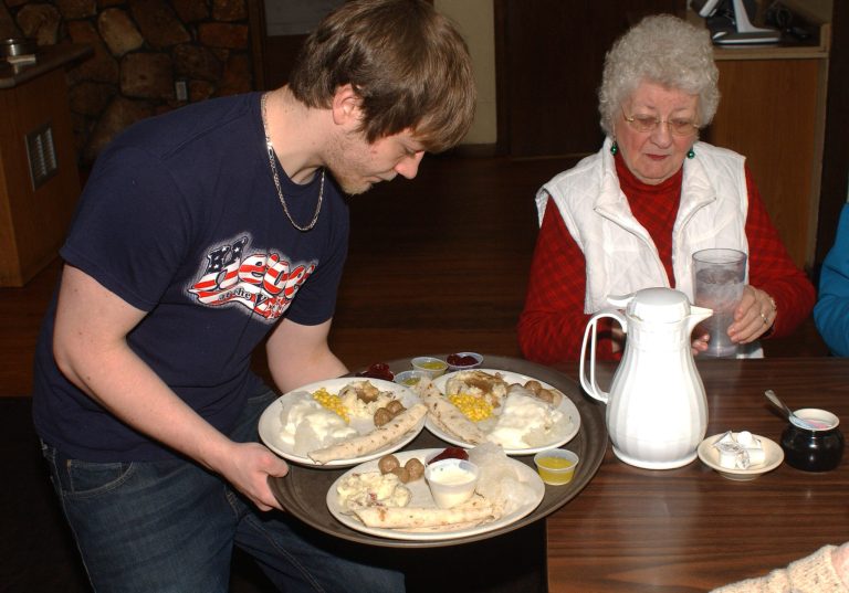   In this Dec. 20, 2012 photo, Ryan Bosma serves lutefisk to Marian Rasmussen at the VFW in Litchfield, Minn. Dozens of Minnesota Scandinavians and the people who love them still flock to the VFW Club in Litchfield every Thursday from November through January, where a $20 bill will get you a big steaming hunk of the frequently mocked fish dish known as lutefisk. (AP Photo/Ron Adams)  