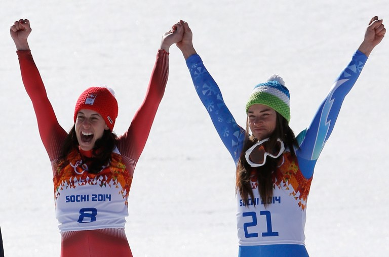 Women's downhill gold medalists Switzerland's Dominique Gisin, left, and Slovenia's Tina Maze, right, hold hands during a flower ceremony at the Sochi 2014 Winter Olympics, Wednesday, Feb. 12, 2014, in Krasnaya Polyana, Russia.  (AP Photo/Christophe Ena)
