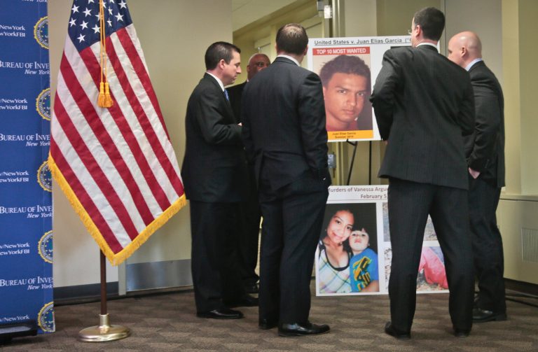 Federal and state law officials confer around a display of Juan Elias Garcia, top center, and his alleged murder victims Vanessa Argueta and her son Diego Torres, bottom center, before a press conference at the FBI's New York field office, Wednesday March 26, 2014. Garcia has been added to the FBI's 