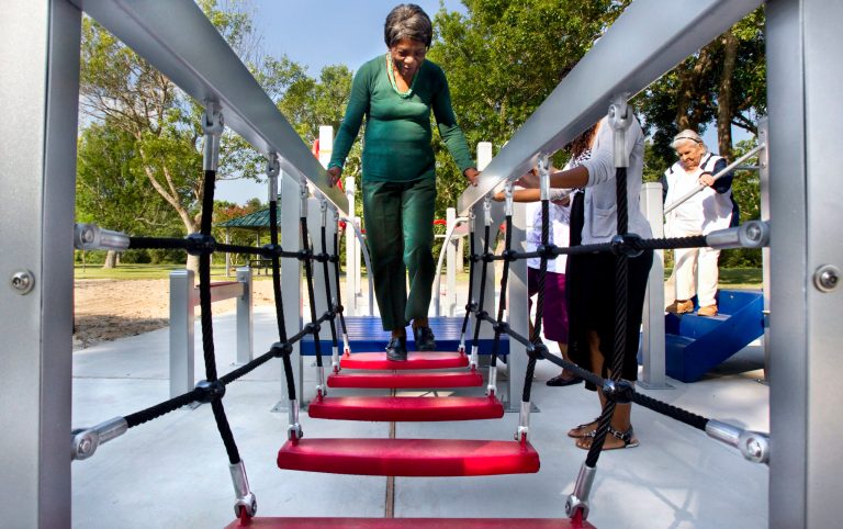 In this photo taken on Wednesday, Aug. 13, 2014, 84-year-old Zady Jones walks across a rope step bridge while trying out the new senior playground at Carbide Park in La Marque, Texas.  The playground will be officially open to the public Thursday, after a ribbon-cutting ceremony. (AP Photo/The Galveston County Daily News, Stuart Villanueva) MANDATORY CREDIT, MAGS OUT, TV OUT