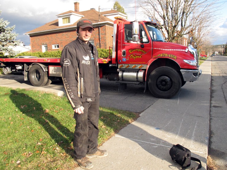   In this Nov. 13, 2012 photo, Nicholas Dostie stands in front of his tow-truck in Magog, Quebec, that he said he used to tow a van in which about a dozen men, women and children entered Canada illegally from the United States and applied for political asylum. Canadian immigration officials on Wednesday, Dec. 5, 2012 said a Romanian smuggling ring has been bringing Gypsies into the U.S. through Mexico in order for them to eventually gain asylum in Canada. (AP Photo/Wilson Ring)  