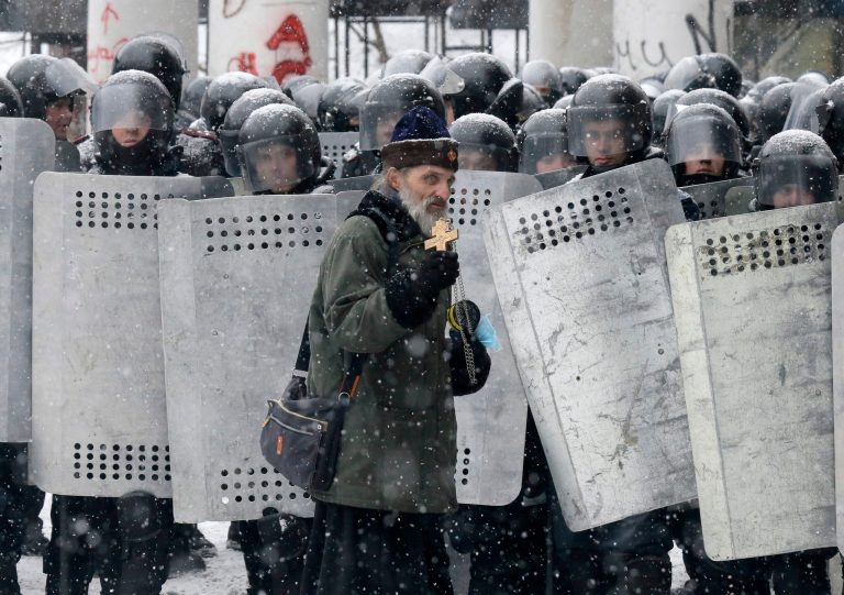 FILE  In this file photo taken on Wednesday, Jan.  22, 2014, an Orthodox priest prays in front of police officers as they block a street after clashes in central Kiev, Ukraine. As a barricade of blazing tires belched thick black smoke, a line of priests stood between angry protesters and ominous riot police. Every freezing morning, priests sing prayers to demonstrators gathered on the Ukrainian capital's main square, a solemn and soothing interlude to vehement speeches calling for revolution.(AP Photo/Efrem Lukatsky, file)