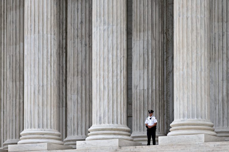In this Oct. 7, 2014, photo, a police officer is dwarfed amid the marble columns of the Supreme Court in Washington. Some warehouse workers who fill orders for Amazon.com customers say they spend up to 25 minutes after every shift waiting to pass through security checks to make sure they aren't stealing from the online retailer. But they don't get paid for the extra time. The Supreme Court hears arguments Wednesday in a lawsuit filed by two former staffers at a Nevada warehouse who claim they should be compensated for time spent in security screenings under the Fair Labor Standards Act.  (AP Photo/J. Scott Applewhite)