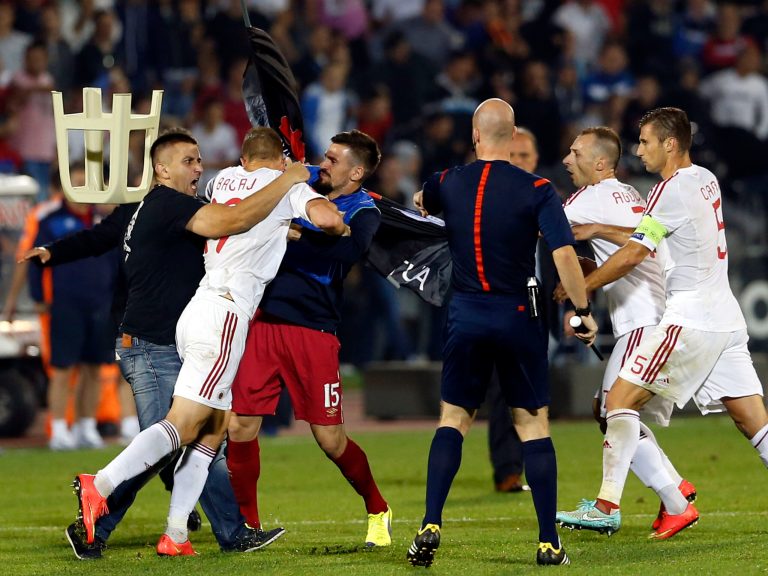 A fight breaks out on the pitch between Serbian fans and Albanian national team players, with from right, Albania's Lorik Cana, Albania's Ansi Agolli, match official, 3rd left Serbia's Nenad Tomovic holding Albanian flag, Albania's Bekim Balaj, and soccer fan at left, during the Euro 2016 Group I qualifying match between Serbia and Albania, at the Partizan stadium in Belgrade, Serbia, Tuesday, Oct. 14, 2014.  The match was suspended on Tuesday after pitch skirmishes involving players and fans over an Albanian flag that was flown above the stadium by a drone.  The score was 0-0 at the time. (AP Photo/Marko Drobnjakovic)
