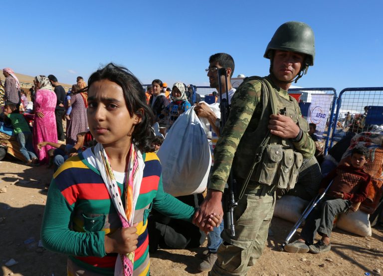 A Turkish soldier holds the hand of Sidra, 12, a Kurdish refugee girl from Kobani who lost her parents after their arrival at the Turkey-Syria border near Suruc, Turkey, Tuesday, Sept. 30, 2014. U.S.-led coalition airstrikes targeted Islamic State fighters pressing their offensive against a Kurdish town near the Syrian-Turkish border on Tuesday in an attempt to halt the militants' advance, activists said. (AP Photo/Burhan Ozbilici)