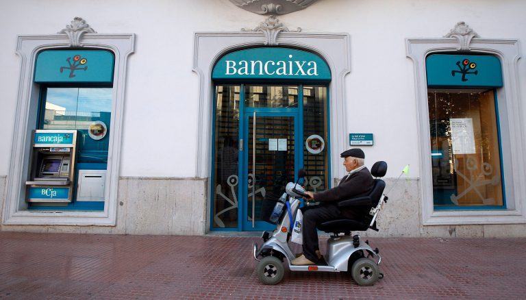   In this photo taken Oct 23, 2012, a disabled man passes a Bancaixa regional savings bank that is now part of Spanish banking giant Bankia in La Vall D'Uixo, near Valencia, Spain. Thousands of townspeople and nearly a million across Spain followed bank manager's advice and invested their life savings in the bank's stocks. Lured by the family-like ties nurtured between bankers and customers, they poured their life's savings into higher-yielding financial instruments recommended by the people managing their money. When boom turned to catastrophic bust, they found the stock they had acquired had become all but worthless. (AP Photo/Alberto Saiz)  