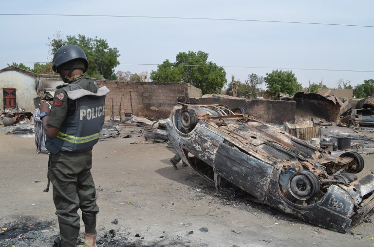 A Nigerian policeman stands guard by burned out cars and houses, following an attack by suspected Islamic extremists in Kawuri, Maiduguri, Nigeria, Tuesday, Jan. 28, 2014. (AP Photo/Jossy Ola)