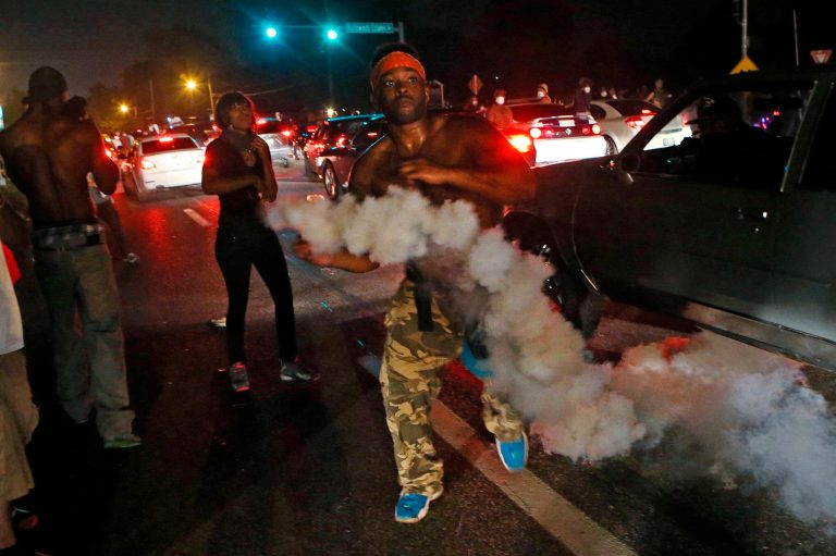 A protester tries to throw tear gas back at the police in Ferguson, Mo., Sunday. Protests over the killing of 18-year-old Michael Brown by a white police officer have entered their second week. (AP Photo/St. Louis Post-Dispatch, J.B. Forbes)