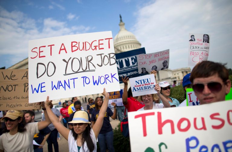 Protestors hold signs during a during an event with the Democratic Progressive Caucus and furloughed federal employees on Capitol Hill in Washington, Friday, Oct. 4, 2013, as the budget battle continued. President Barack Obama decided to stay home from economic summits in Asia as Democrats stepped up pressure on congressional Republicans to rein in their tea party faction and reopen the government with no strings attached.  (AP Photo/ Evan Vucci)