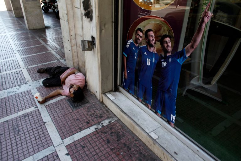   A man begging for alms lays by a sticker with Greece' national football team players one day before general elections in Athens, on Saturday, June 16 2012. Greeks vote for the second time in six weeks Sunday amid fears that the country could be forced out of the euro if they reject the strict austerity measures taken in return for billions of euros in rescue loans from other European countries and the International Monetary Fund. (AP Photo/Kostas Tsironis)  