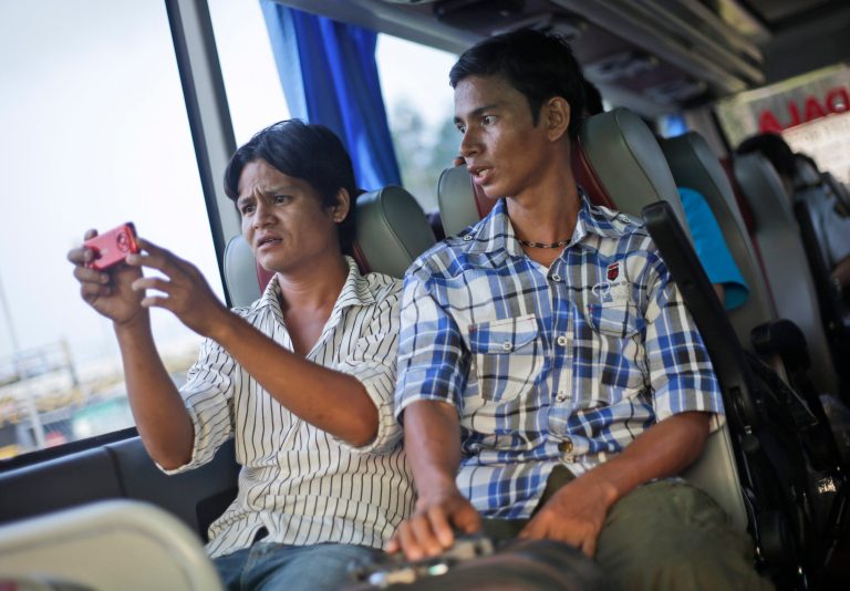 In this March 11, 2014 photo, Burmese trafficking victims Min Min Chan, right, watches as his friend Kya Wue shoots video with his mobile phone on a bus that takes them to their transit hotel wait for their bus before returning to their country at Soekarno-Hatta International Airport in Jakarta, Indonesia. Tens of thousands of invisible migrants are trafficked annually through Thailand, Southeast Asia's second-largest economy. (AP Photo/Dita Alangkara)